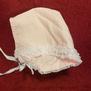 Light pink colored infant hat with lace edging and ribbon tie. 6M